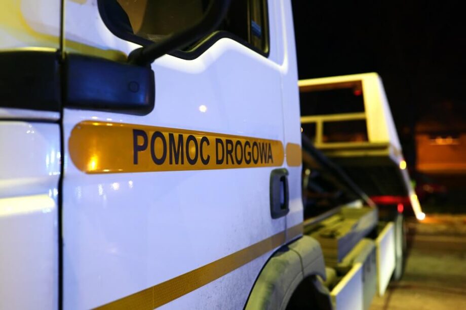 Biała ciężarówka z napisem pomoc drogowa 24h widoczna w nocy.